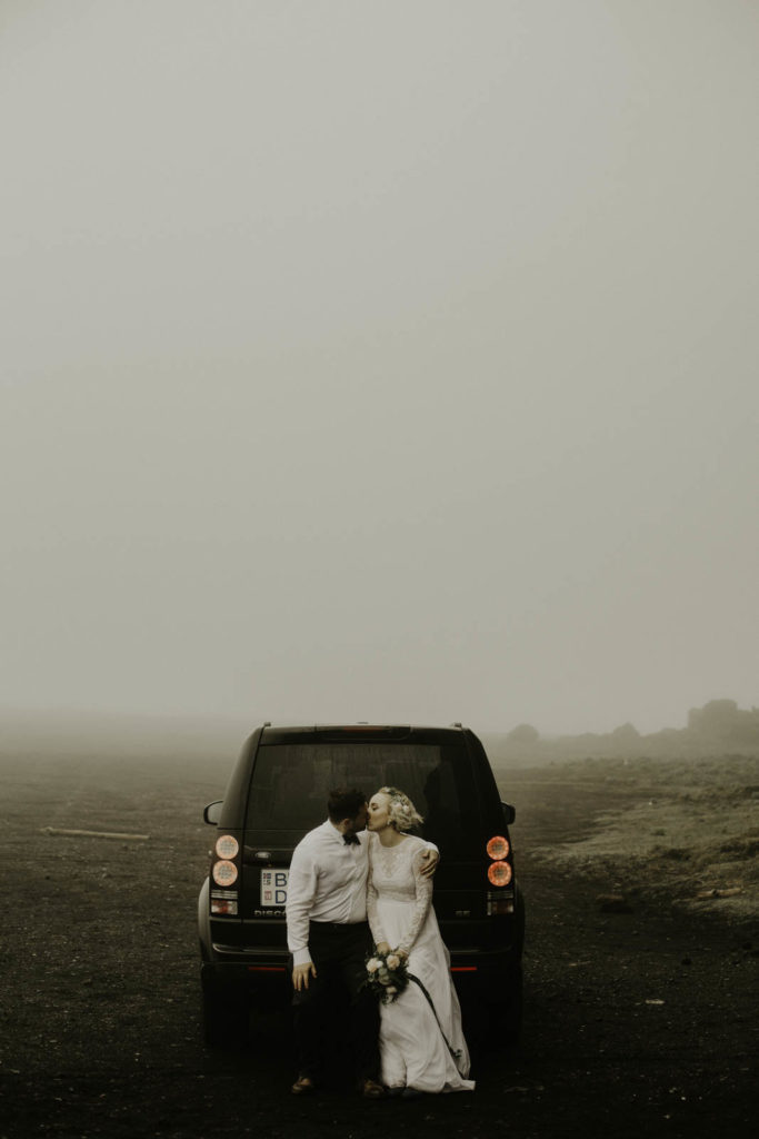 bride and groom sitting on car in fog
