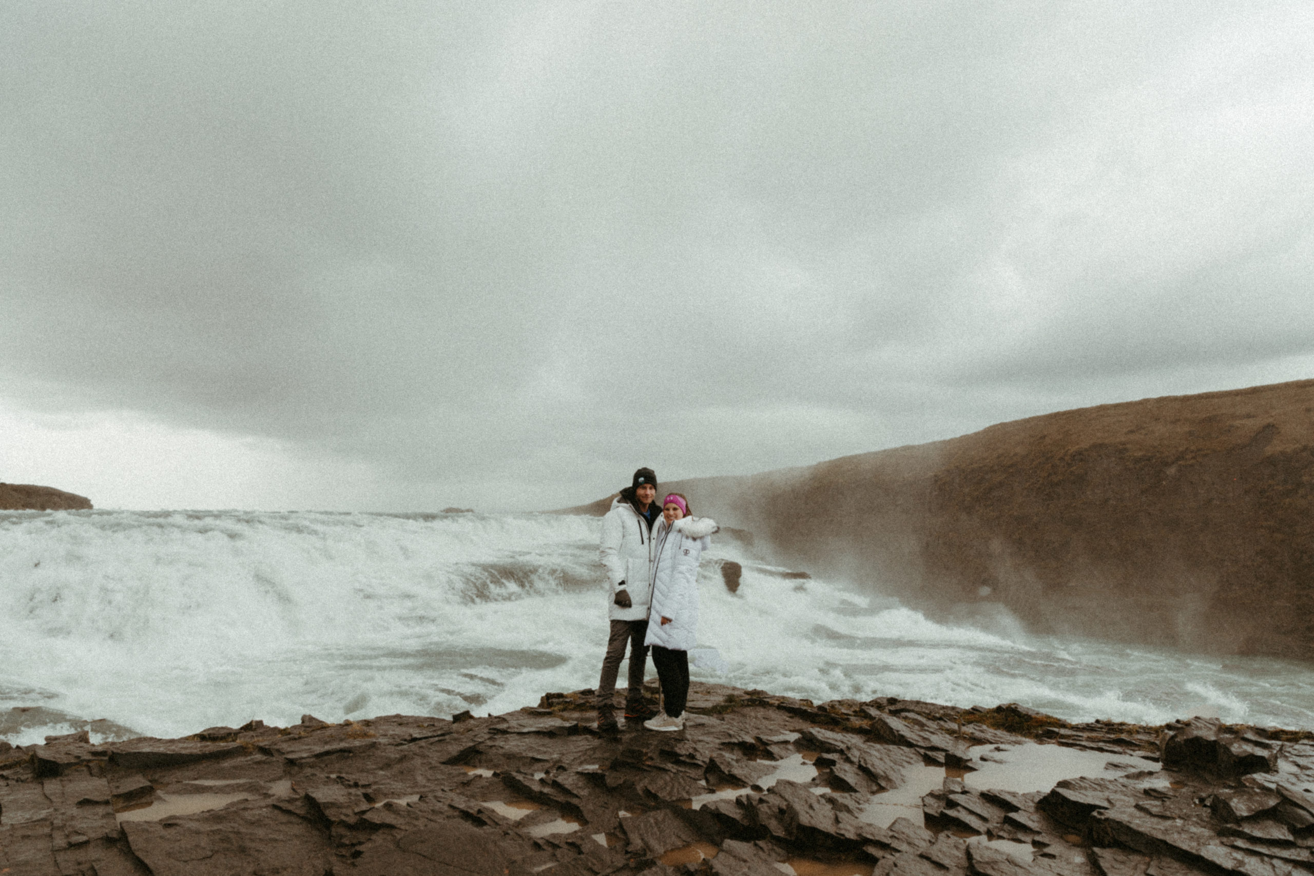 Bride and Groom wearing matching white puffy coats in iceland at Gullfoss in golden circle.