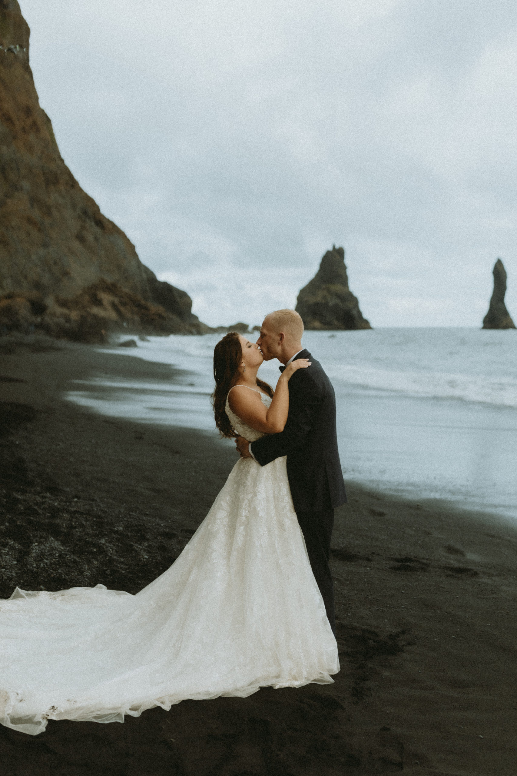 bride and groom kissing on black sand beach on wedding day in iceland. 