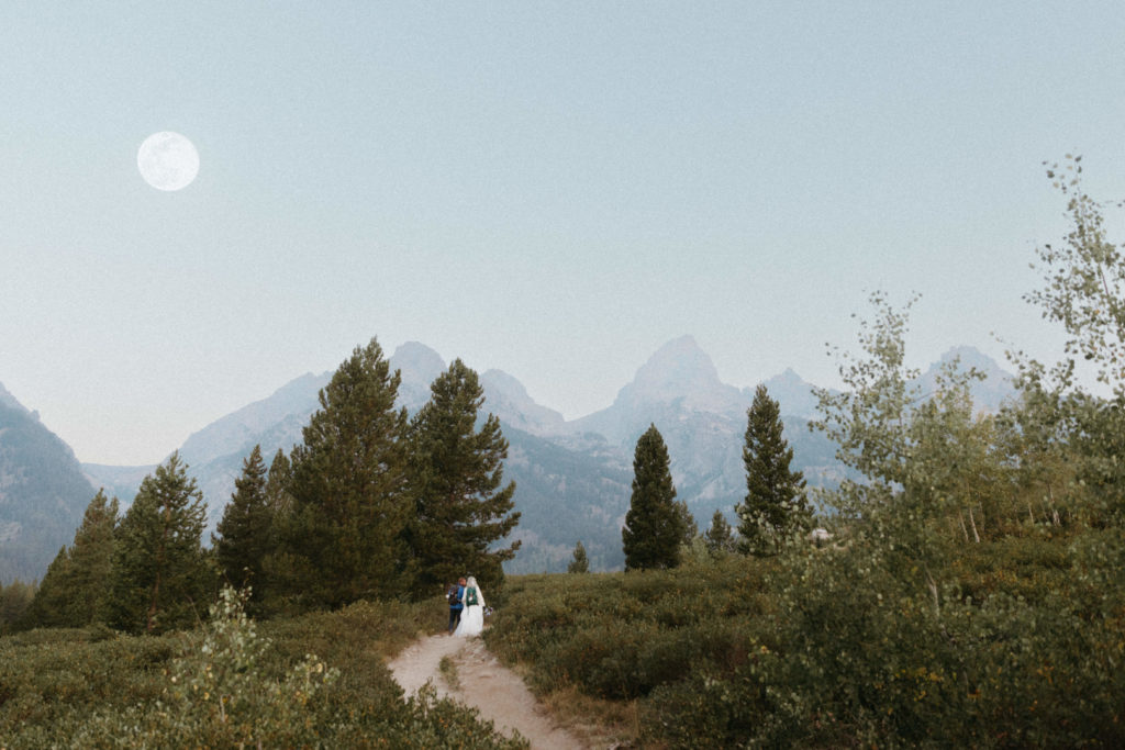 Bride and groom hiking on trail during a full moon in Grand Teton national park.