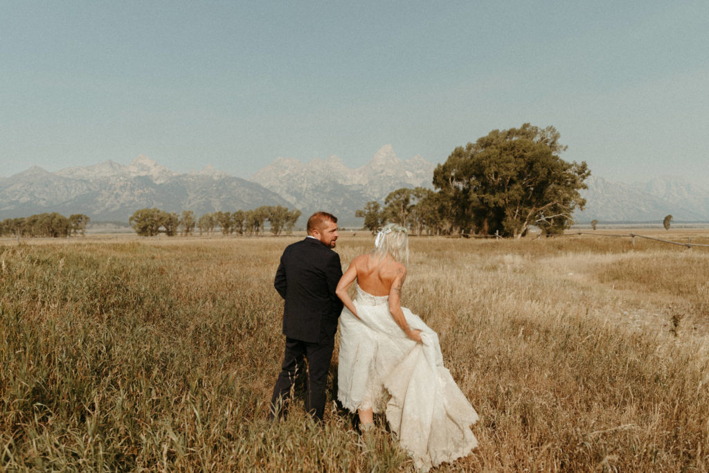 Bride and groom in a golden field with the Grand Teton Mountains behind them. 