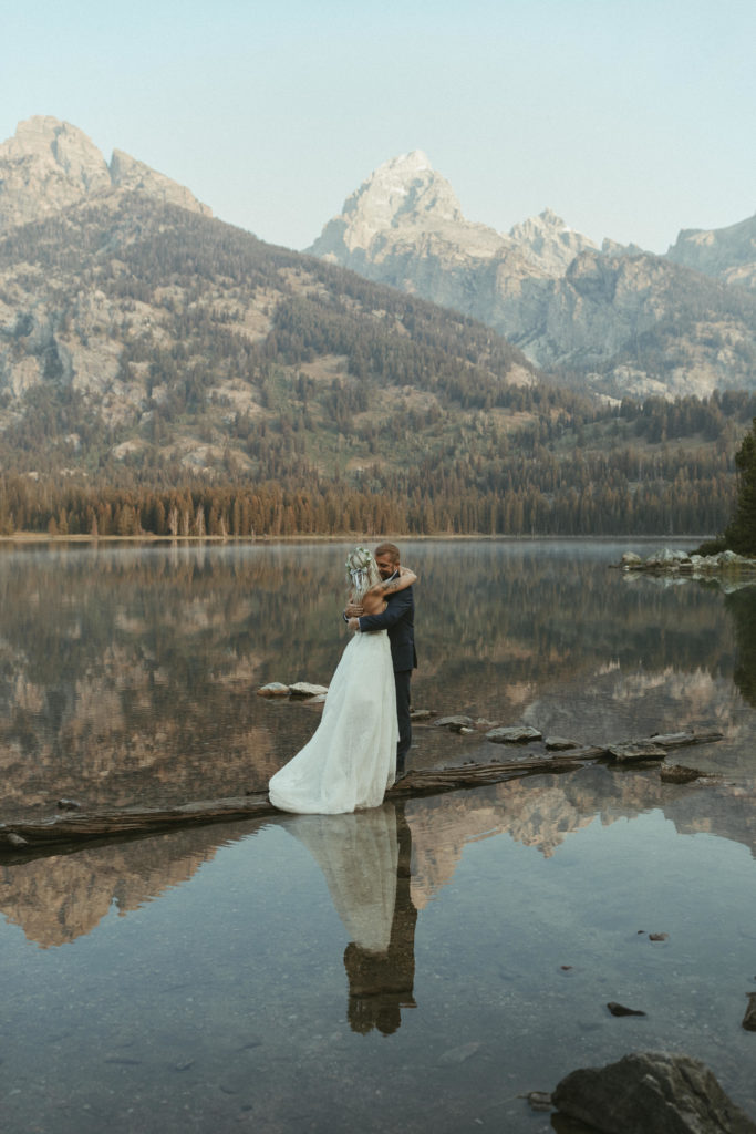 Bride and groom kissing in front of lake and mountains.