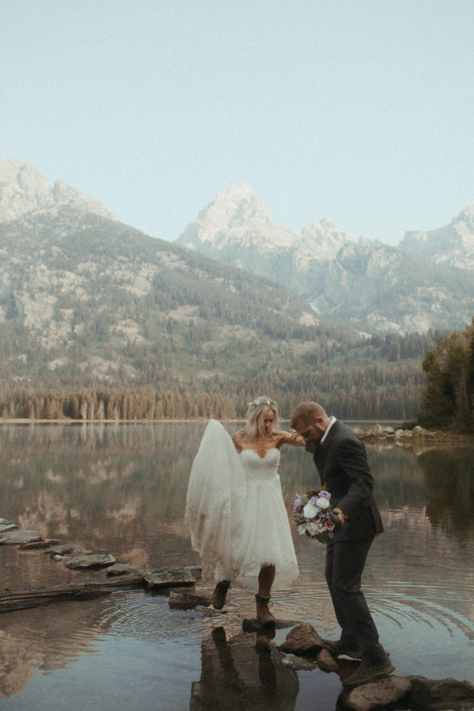 Bride and groom hiking in front of lake and mountains.