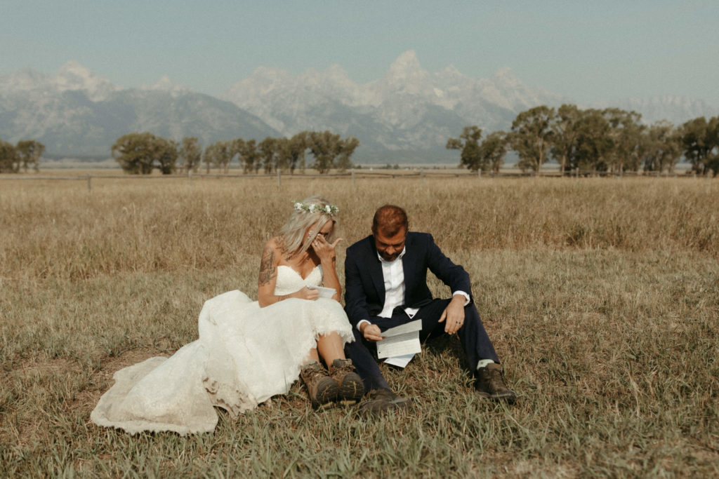 bride and groom reading vows in golden field with mountains behind them.